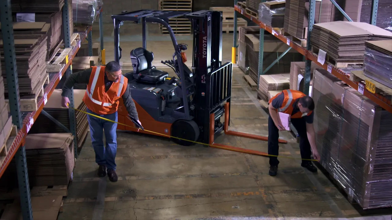 Two men measuring the floor next to a parked Toyota-Core Electric Turret Forklift in a warehouse